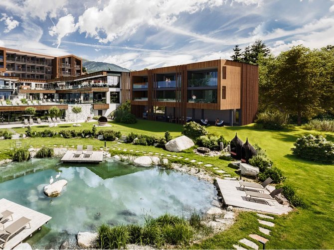 Willkommen in der Ferienregion Gitschberg Jochtal! Moderner Hotelkomplex mit Teich und Liegestühlen in grüner Landschaft
