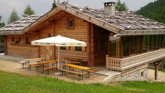 Rund um Meransen: Hütten und Almen Rustikale Holzhütte mit Außenbänken und Sonnenschirm in einer grünen Landschaft