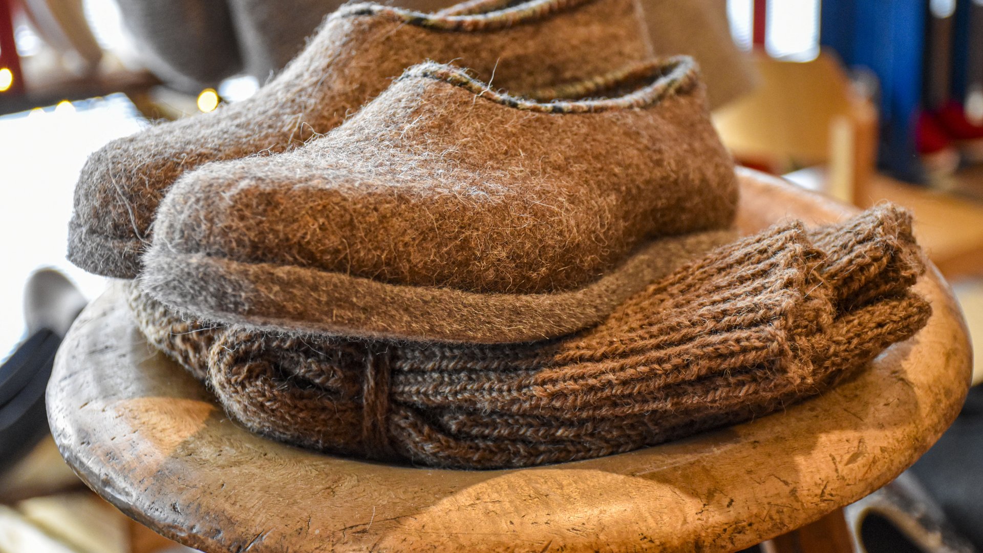 Advent in Terenten The picture shows a pair of grey felt slippers lying on a stool. Under the slippers there is a folded, thick knitted sweater, all with a cozy and handmade look.