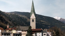 Mühlbach in the Pustertal valley Church tower with green spire against forested mountains and houses