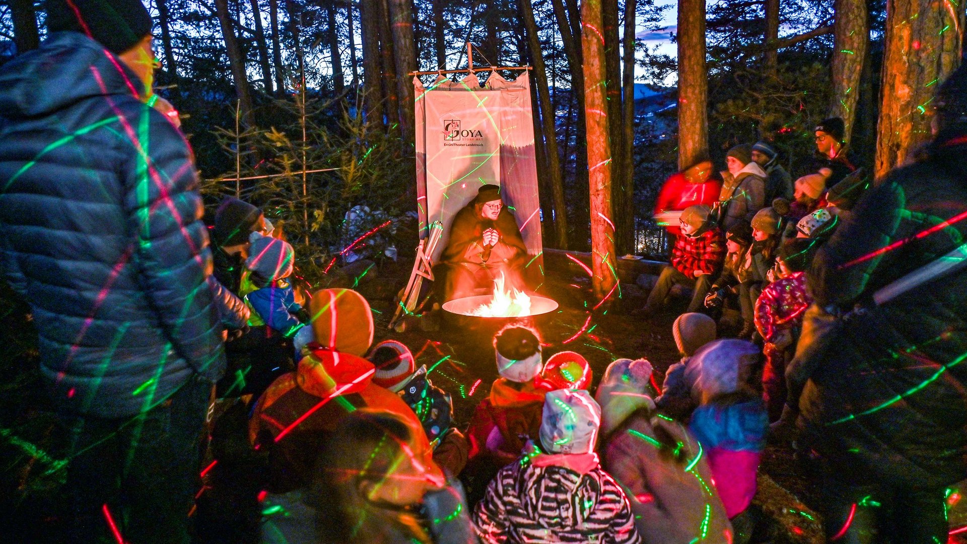 Tearna Advent Kinder und Erwachsene hören einer Person bei einer Lagerfeuergeschichte im Wald zu