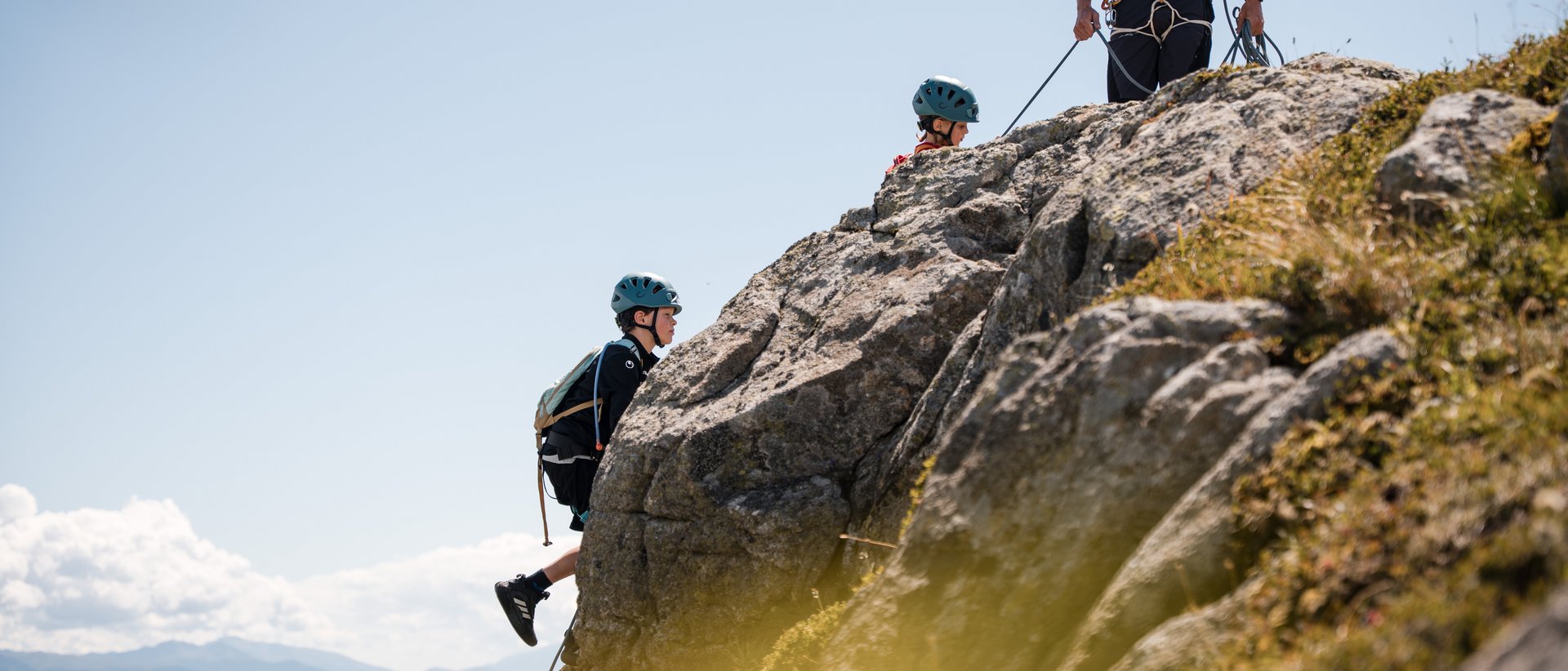 Euer Familienurlaub in Südtirol Kinder klettern mit Helm und Sicherheitsausrüstung auf Felsen mit Bergkulisse
