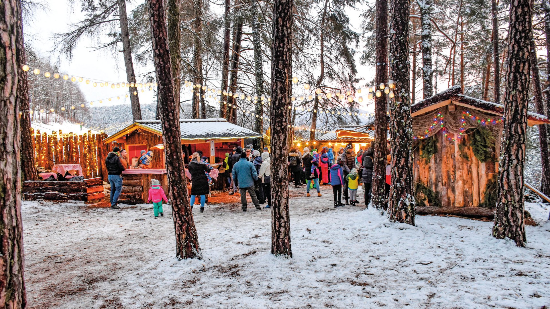 Tearna Advent Menschen bei einem beleuchteten Wintermarkt im schneebedeckten Wald