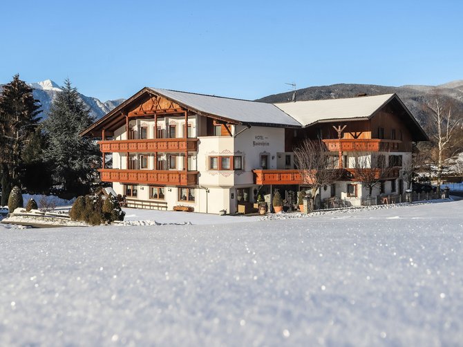 Willkommen in der Ferienregion Gitschberg Jochtal! Hotel im Schnee mit Bergen im Hintergrund bei klarem Himmel