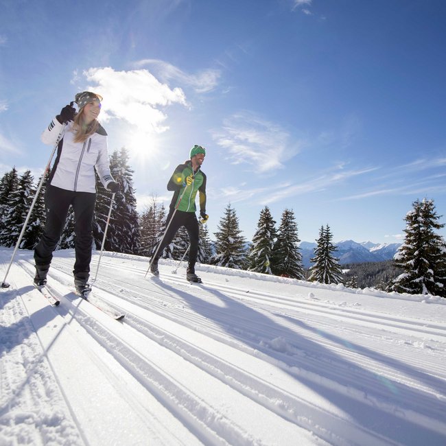 Cross-country skiing in Italy: discover Gitschberg Jochtal Two people cross-country skiing on snowy trail in bright sunlight