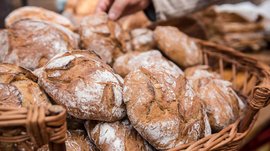 Winkelen in Mühlbach/Italië De afbeelding toont een mand vol versgebakken broden met een knapperige korst en licht bebloemd oppervlak. Een hand grijpt naar een van de broden, wat duidt op een verkoop of een keuze.