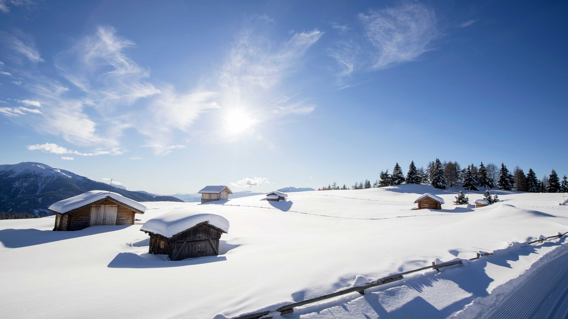 Langlauf auf der Rodenecker-Lüsner Alm Verschneite Holzhütten auf sonnigem Berg mit blauem Himmel