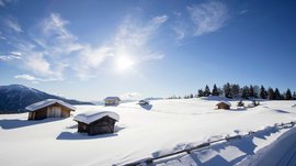 Langlauf auf der Rodenecker-Lüsner Alm Verschneite Holzhütten auf sonnigem Berg mit blauem Himmel