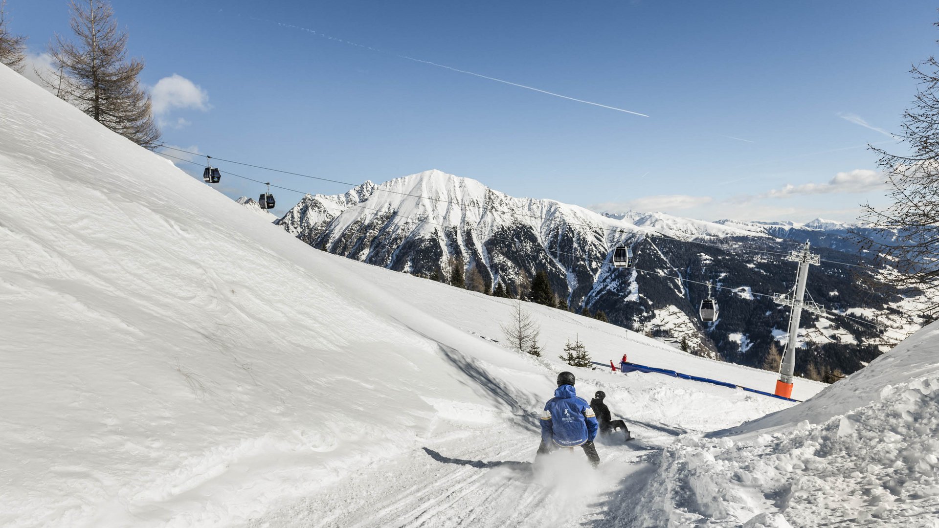 Lyžařská oblast Gitschberg Jochtal Lidé sáňkují na zasněženém svahu se sedačkovou lanovkou a horami v pozadí