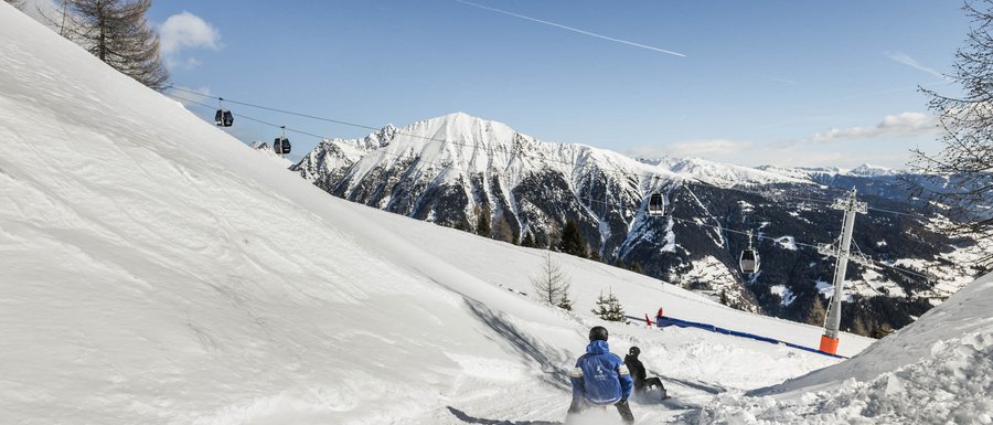 The Gitschberg webcams People sledding on snowy slope with cable cars and mountains in background