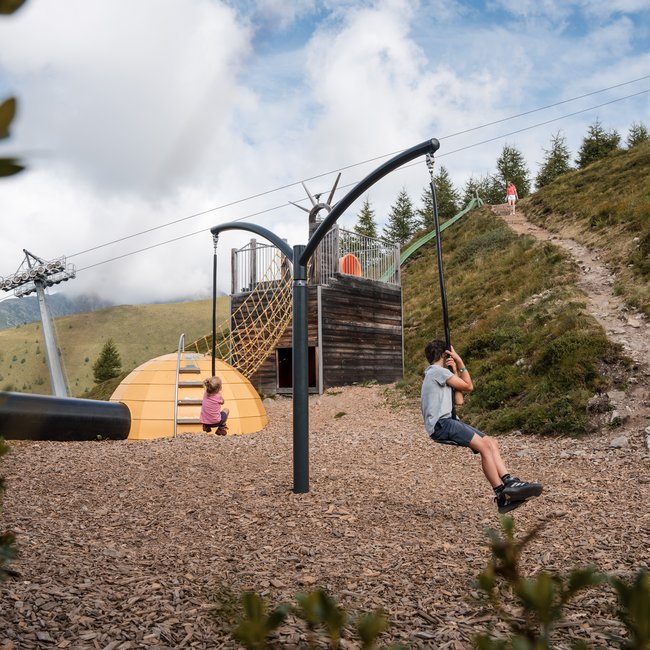 Südtiroler Almkost Kinder spielen auf Seilrutsche in Bergspielplatz mit Rutsche und Kletternetz