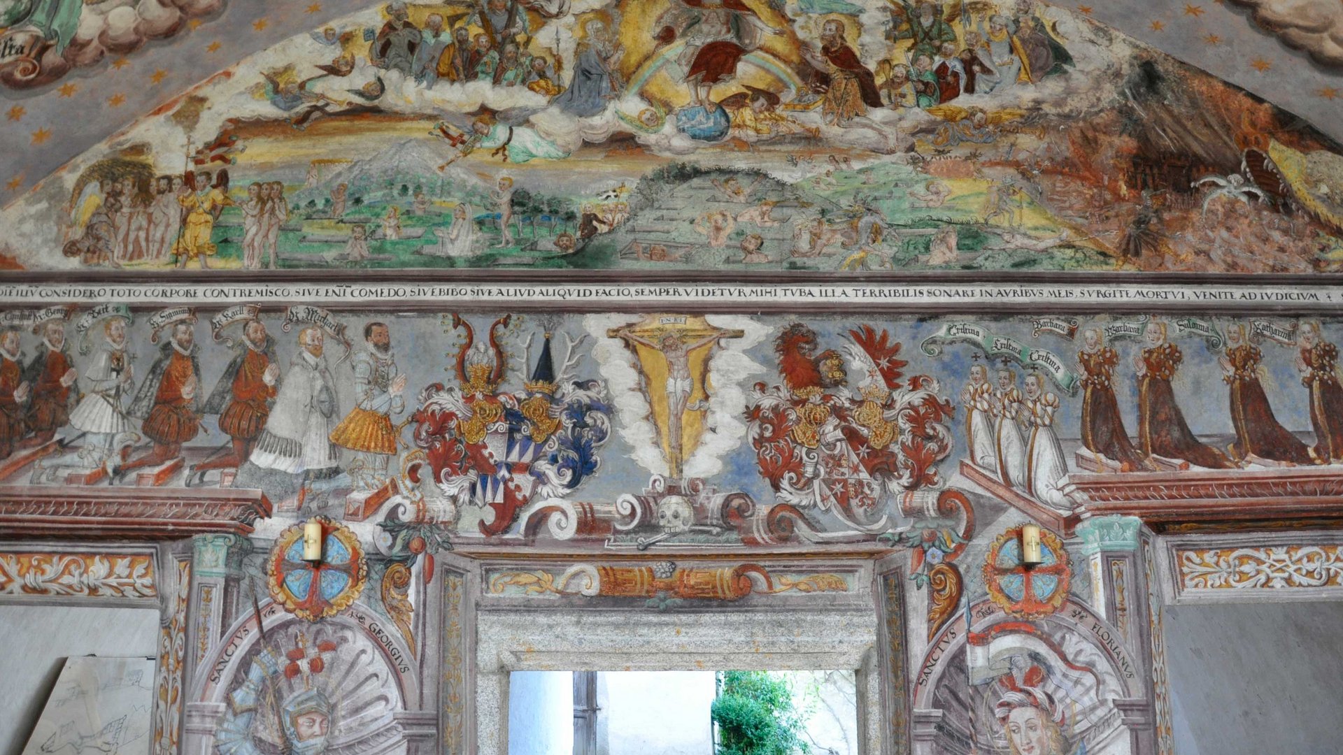 Mächtig und erhaben: Schloss Rodenegg Das Bild zeigt ein detailliertes Wandfresko in einem historischen Raum, das religiöse und adelige Figuren sowie Wappen darstellt. Die Szenen sind farbenfroh und reich verziert.