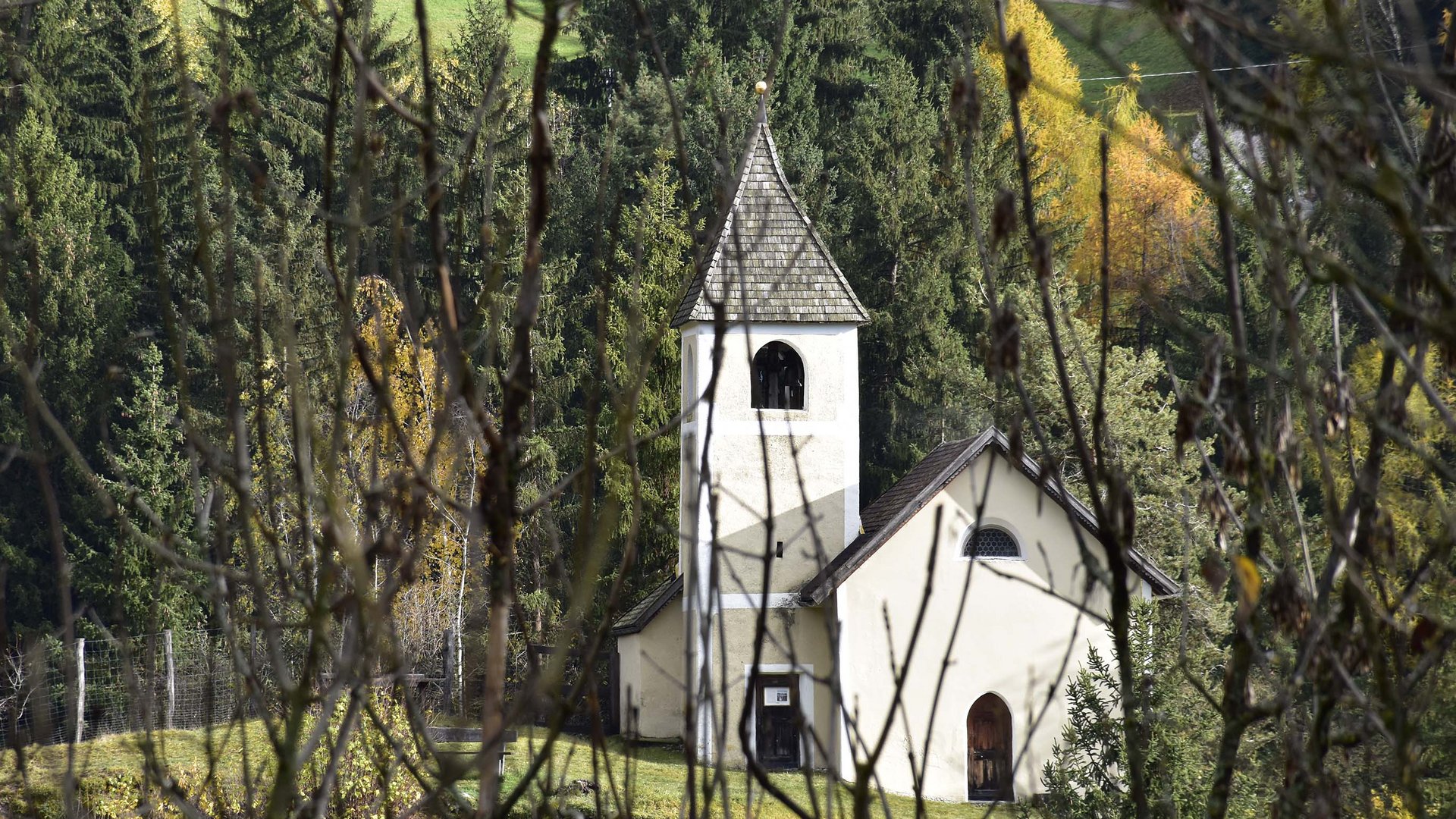 Terenten im Pustertal Kleine Kapelle hinter Büschen vor einem Wald im Herbst
