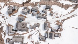 Fane Alm – South Tyrol’s most idyllic Alpine village The image shows a bird's-eye view of a small mountain village with snow-covered wooden roofs. Between the buildings, snowy paths and some exposed brown areas are visible, dominating the winter landscape.