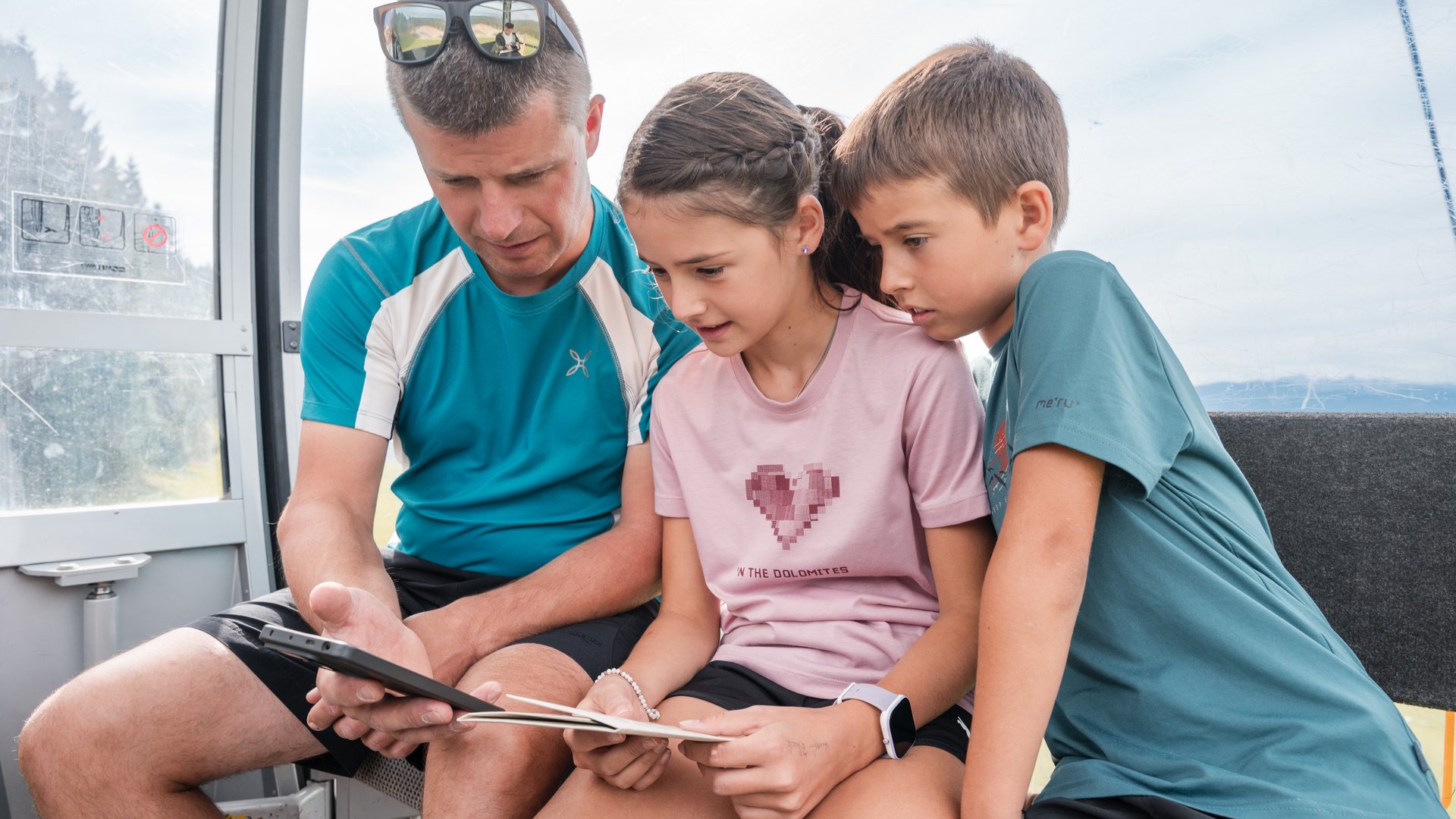 Outdoor Escape on Mt. Gitschberg Man and two kids looking at a smartphone together in a chairlift