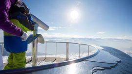 The Gitschberg panoramic platform in Meransen, Italy People looking through binoculars at snowy mountain landscape in bright sunlight
