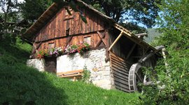 Der Mühlenweg in Terenten Altes Holzhaus mit Wasserrad und Blumen auf dem Fensterbrett in grüner Landschaft