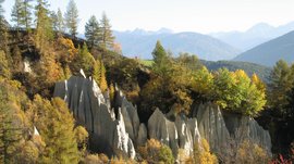 Zemní pyramidy v Terentenu Zemní pyramidy obklopené podzimními stromy a horami v pozadí