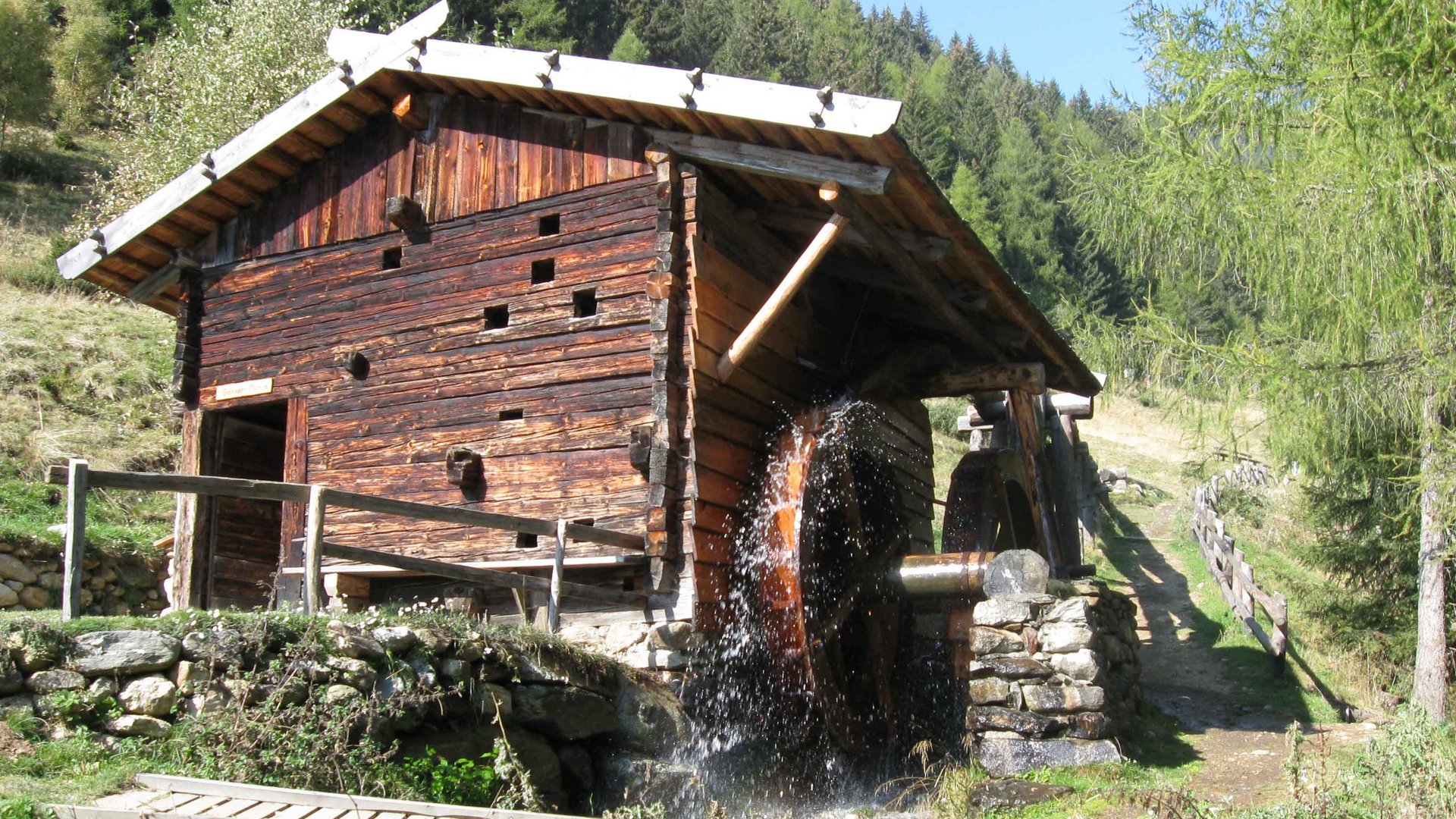 Der Mühlenweg in Terenten Holzmühle mit Wasserrad in bewaldeter Berglandschaft