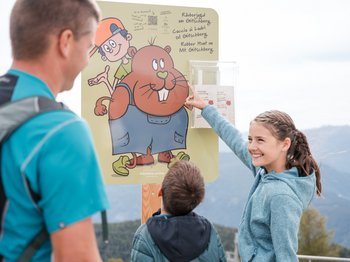 Das Bergdorf Meransen Familie liest Info-Tafel für Räuberjagd am Gitschberg im Freien