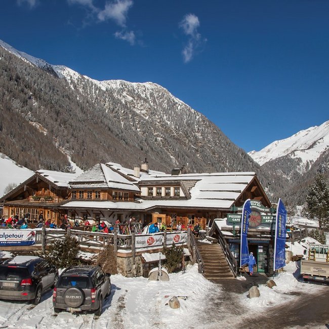 Restaurant Pizzeria Die Mühle Houten gebouw in besneeuwd Alpenlandschap met geparkeerde auto's en skispullen