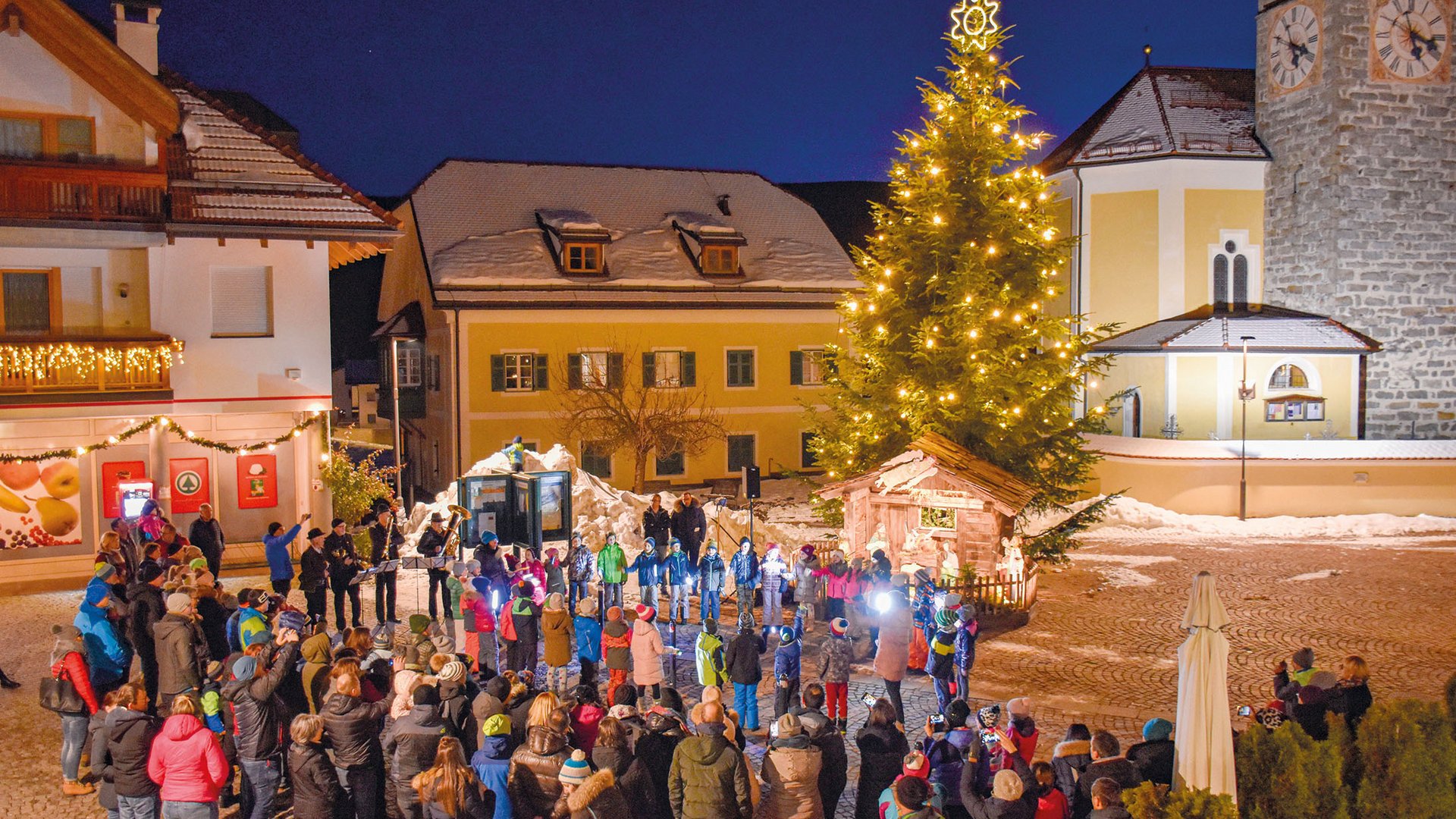 Tearna Advent Weihnachtsbaum mit Beleuchtung und Menschen, die eine Feier auf dem Marktplatz beobachten