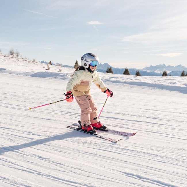 Skiurlaub mit Kindern in Südtirol Kind fährt Ski auf verschneiter Piste mit Bergen im Hintergrund