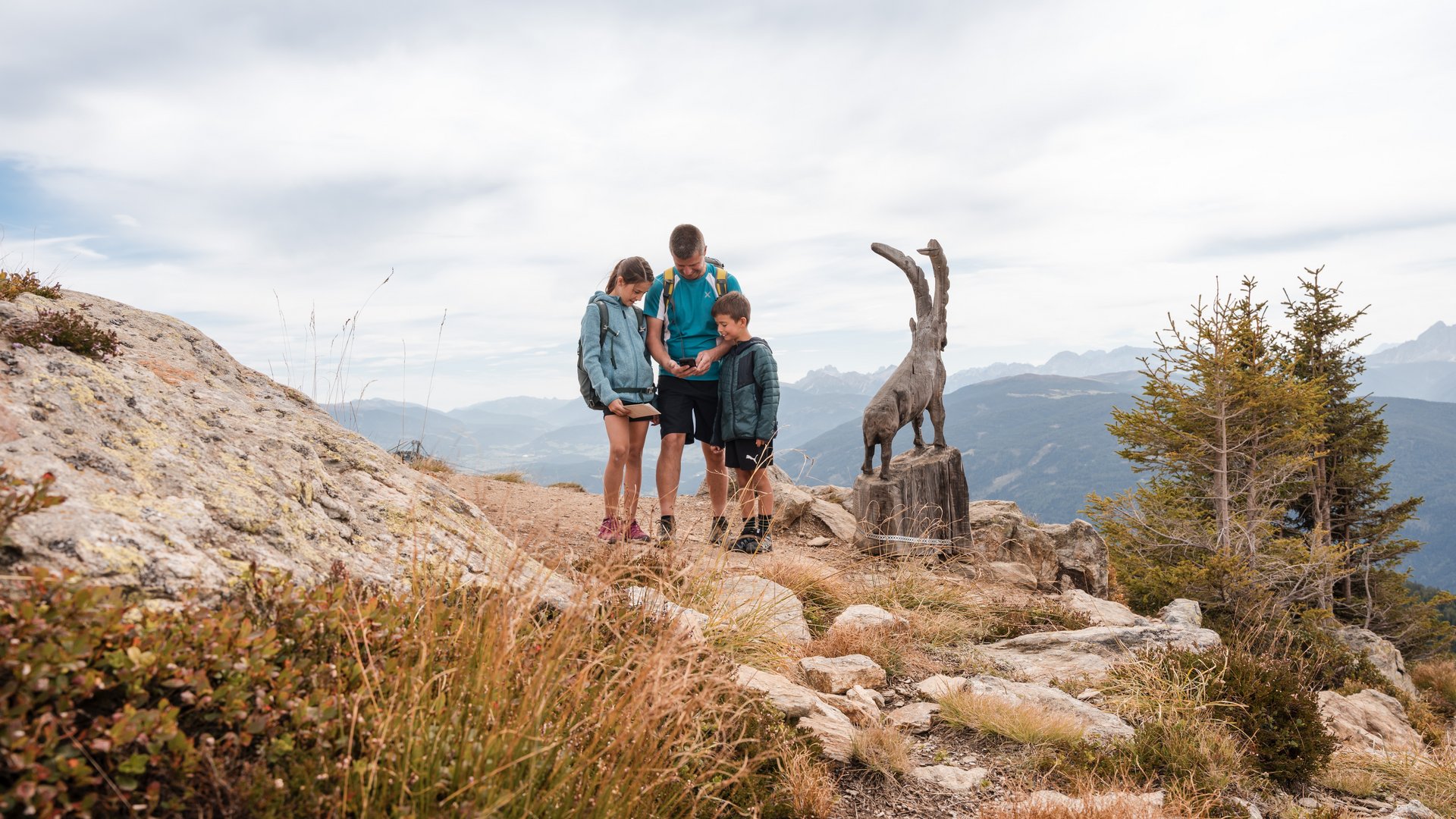 Outdoor Escape on Mt. Gitschberg Family looking at map near wooden goat sculpture in mountains