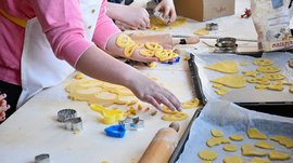 Advent in Terenten The picture shows people making cookies from dough using cookie cutters. On a table, there are dough scraps, cookie cutters, and a rolling pin, while the cut-out cookies are being prepared on a baking sheet.