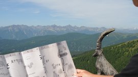 Das Outdoor Escape am Gitschberg Person hält Karte mit Bergblick und Holzskulptur einer Ziege