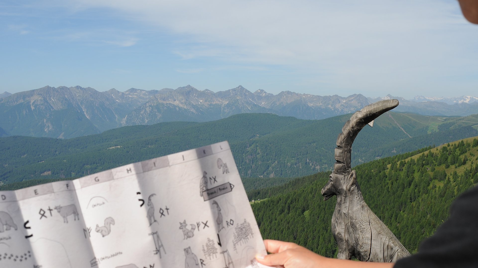 Das Outdoor Escape am Gitschberg Person hält Karte mit Bergblick und Holzskulptur einer Ziege