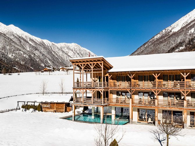 Willkommen in der Ferienregion Gitschberg Jochtal! Hotel mit Außenpool im Schnee in den Bergen unter klarem blauen Himmel
