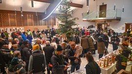 Tearna Advent Menschen auf Weihnachtsmarkt mit Tannenbaum und Ständen in einer Halle