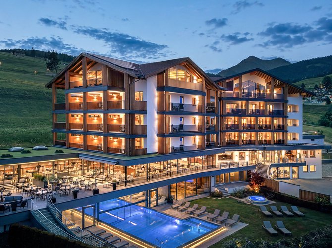 Willkommen in der Ferienregion Gitschberg Jochtal! Beleuchtetes Hotel mit Außenpool und Liegestühlen in den Bergen bei Abenddämmerung