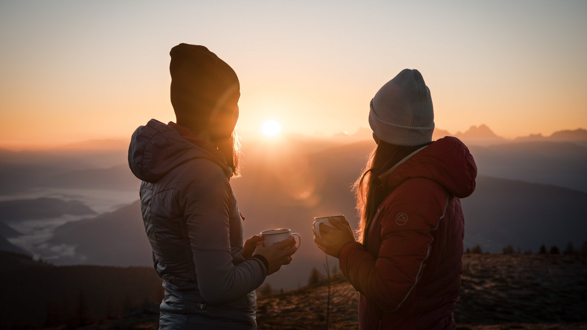 Brixen Südtirol Card: Gästekarte mit kostenlosen Bergbahnen, Mobilität und freien Eintritten Zwei Frauen genießen bei Sonnenaufgang heißen Tee in den Bergen