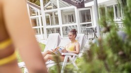 Der Alpinpool in Meransen Eine junge Frau im gelben Bikini auf einem Liegestuhl die eine Zeitschrift liest