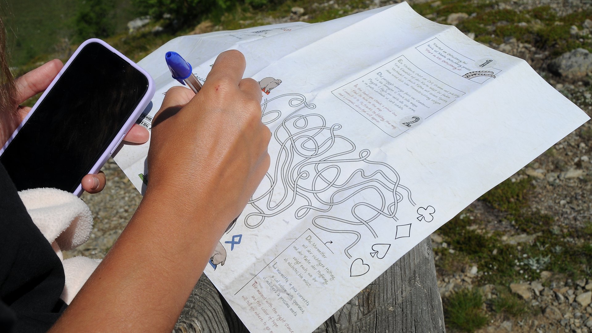 Das Outdoor Escape am Gitschberg Person hält Handy und Stift, löst Labyrinth auf Papier im Freien