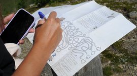 Das Outdoor Escape am Gitschberg Person hält Handy und Stift, löst Labyrinth auf Papier im Freien