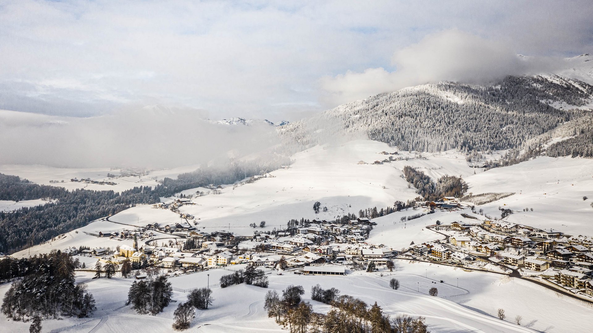Terenten im Pustertal Schneebedecktes Dorf in den Alpen mit Bergen und Wolken im Hintergrund