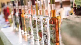 Winkelen in Mühlbach/Italië De afbeelding toont een rij flessen met verschillende sterke dranken, dicht naast elkaar opgesteld. Elke fles heeft een etiket met verschillende motieven en teksten die wijzen op verschillende smaken of ingrediënten.