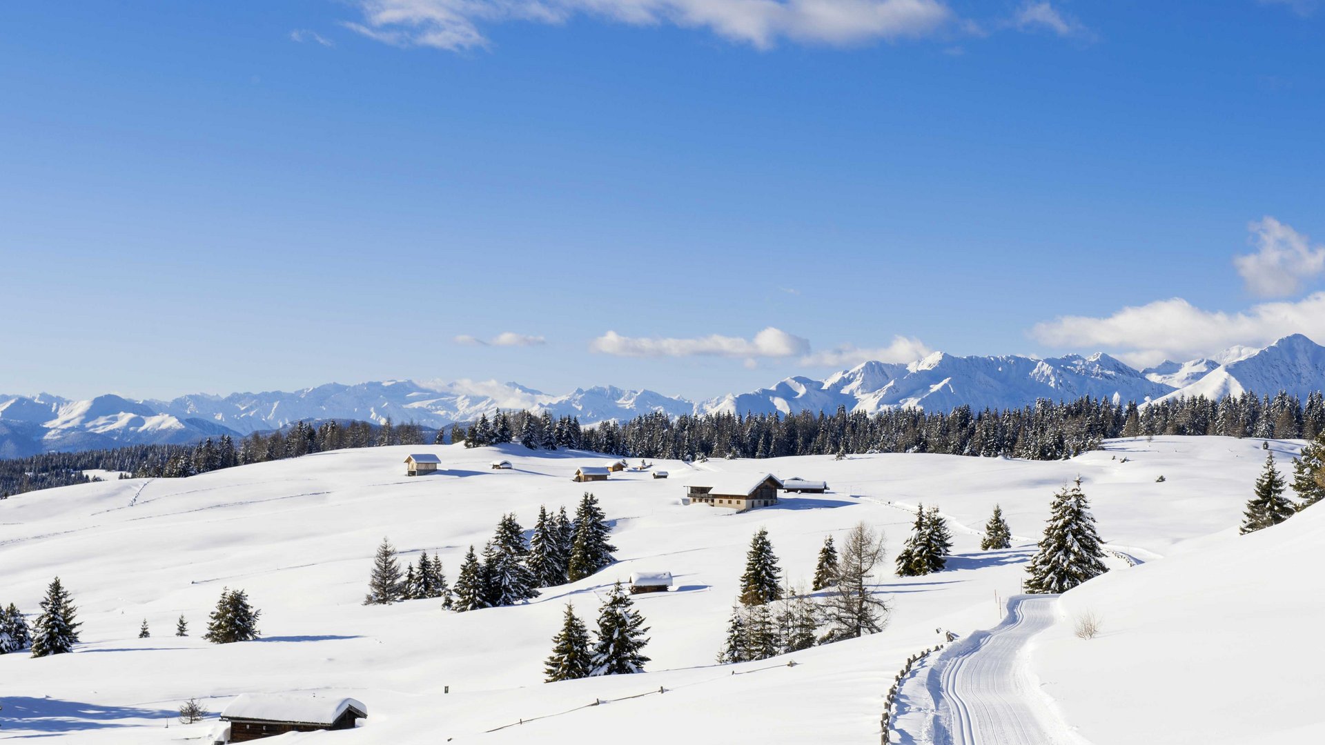 Langlauf auf der Rodenecker-Lüsner Alm Schneebedeckte Berge mit Häusern und Bäumen unter blauem Himmel