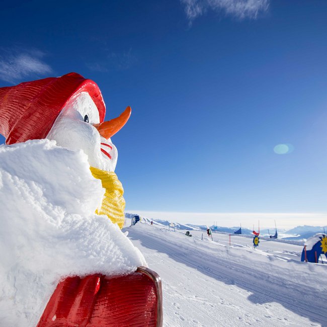 Zimní dovolená s dětmi v Jižním Tyrolsku Velká sněhová postava s červenou čepicí a šálou na zasněženém kopci