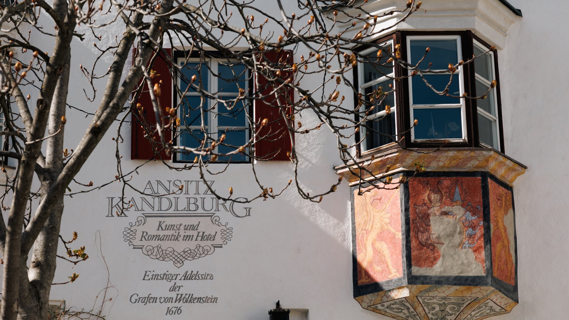 Mühlbach in the Pustertal valley Frescoed balcony and windows on historic white building with tree in front