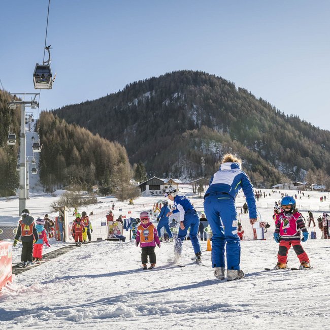 Find your hotel near Brixen! Children learning to ski on a snowy beginner slope with instructors