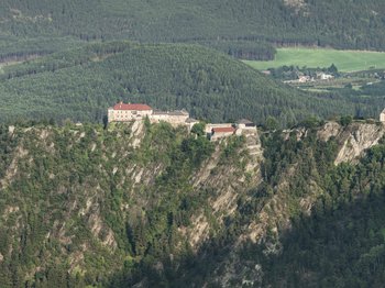 Rodeneck: idyllisches Wanderparadies Das Bild zeigt eine Burg und eine Kirche, die auf einem steilen Felsen thronen. Beide Gebäude sind von üppigem, grünem Wald umgeben, der sich über die umliegenden Hügel erstreckt.