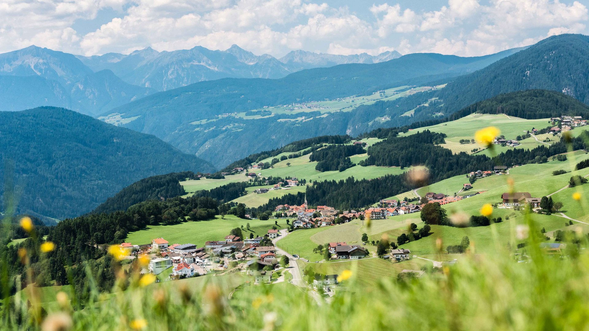 Terenten im Pustertal Blick auf ein Dorf in hügeliger grüner Landschaft mit Bergen im Hintergrund