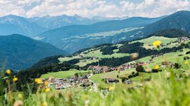 Terenten im Pustertal Blick auf ein Dorf in hügeliger grüner Landschaft mit Bergen im Hintergrund