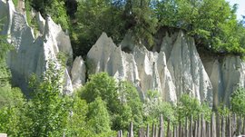 Zemní pyramidy v Terentenu Skalní útvary s dřevěným plotem a zelenými stromy na slunci