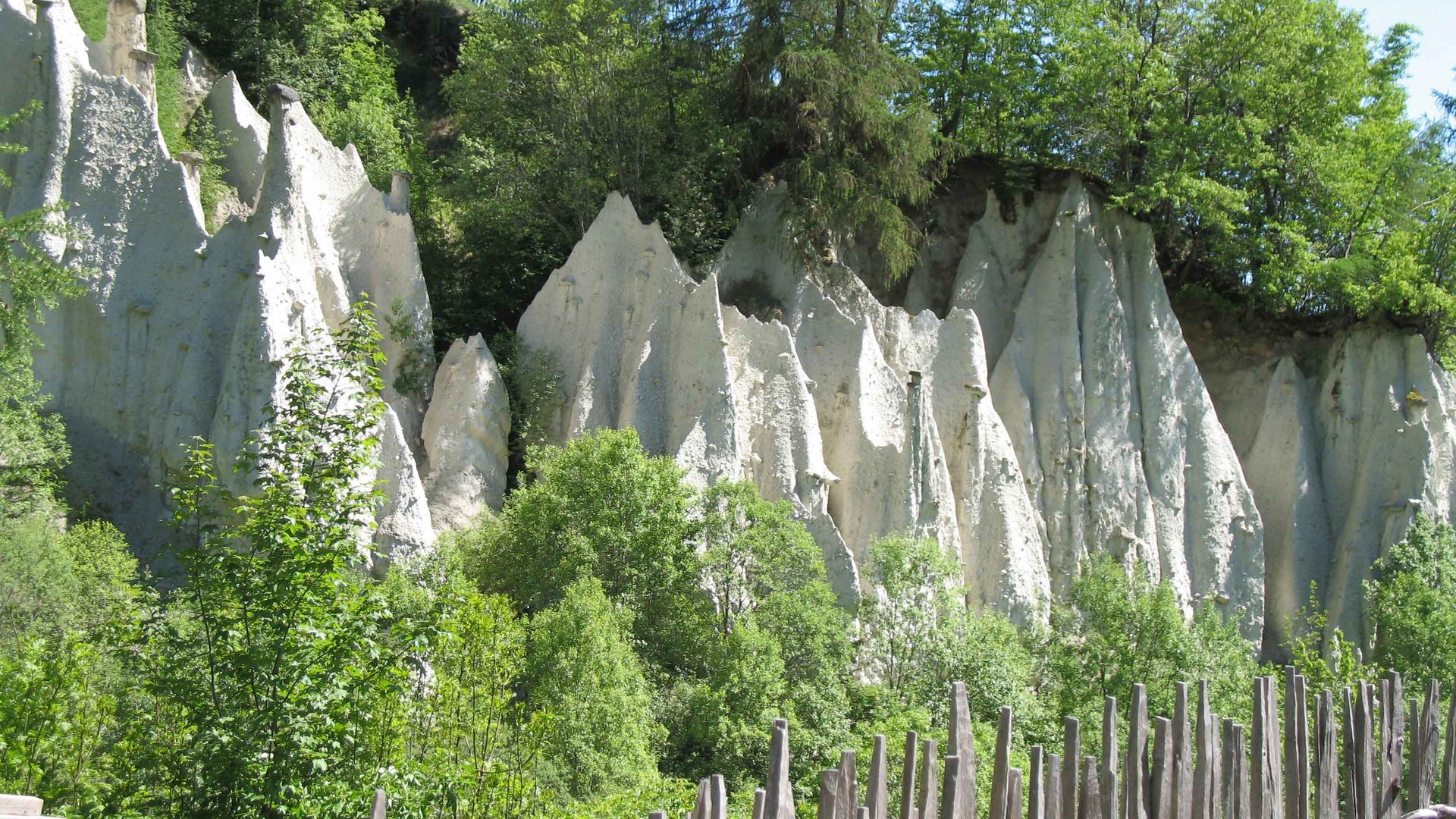 Zemní pyramidy v Terentenu Skalní útvary s dřevěným plotem a zelenými stromy na slunci