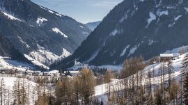 Pfunders: urig und idyllisch Das Bild zeigt ein verschneites Tal mit Bergen im Hintergrund. In der Mitte des Bildes befindet sich ein Dorf, das teilweise von Wäldern umgeben ist. Eine Kirche mit einem markanten Turm ist gut sichtbar im Dorfzentrum.